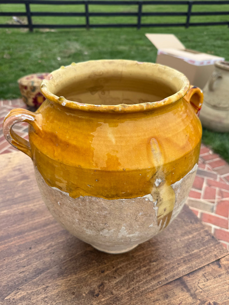 Antique Glazed Yellow ceramic pot on a wooden surface with a grassy area and fence in the background