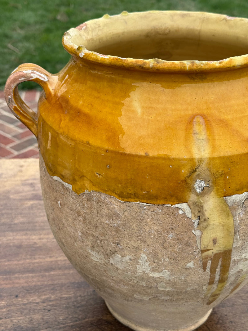 Antique ceramic pot with a yellowish-brown glaze on a wooden surface