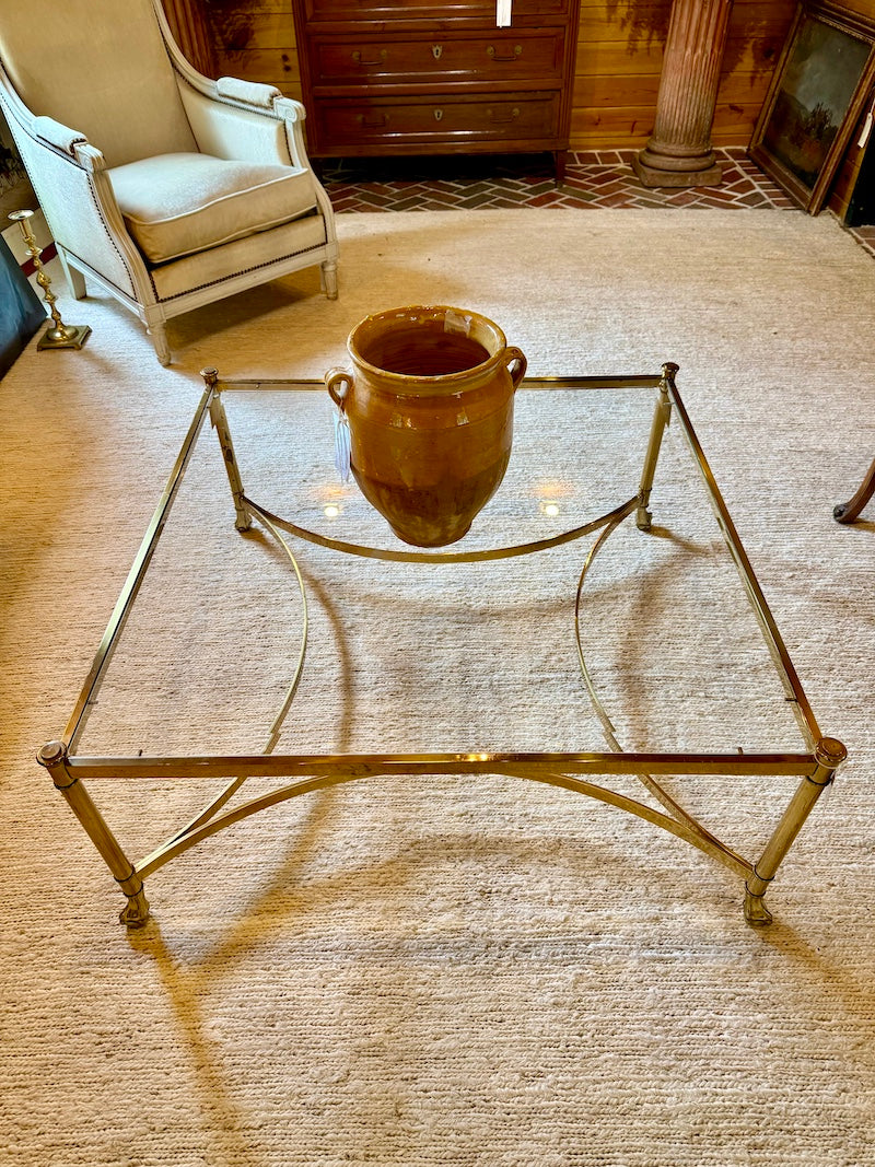 Brass and Glass coffee table with a decorative pot on a textured carpeted floor.