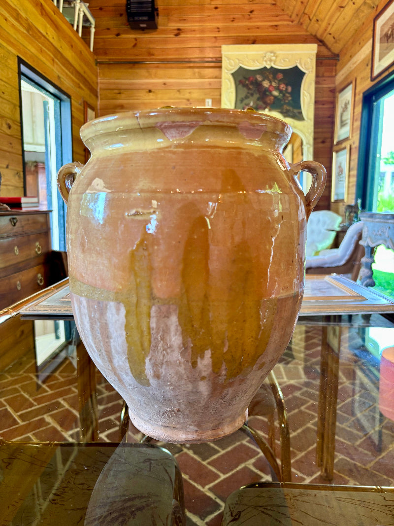Antique French ceramic jar on a glass table in a room with wooden walls and furniture.