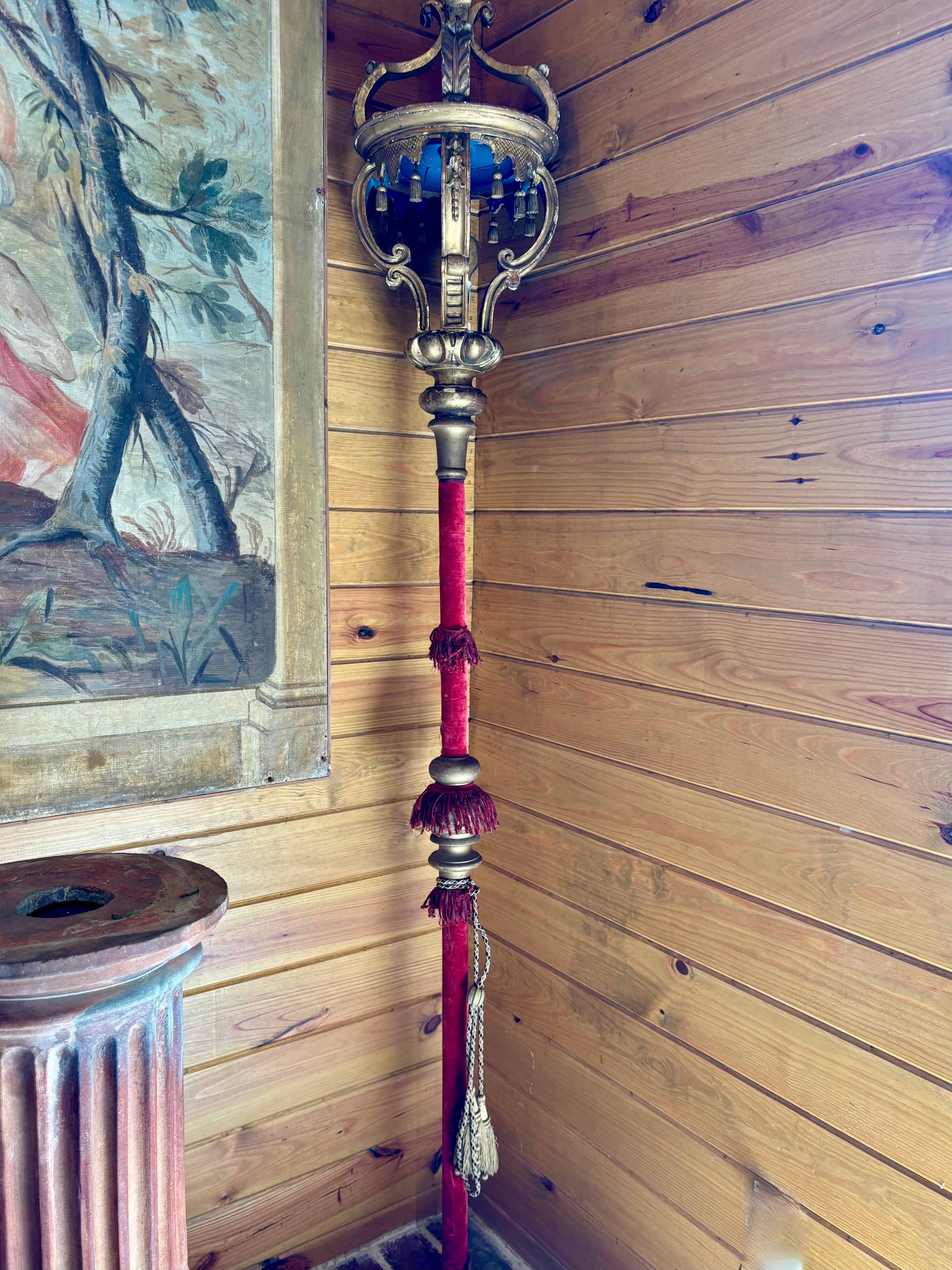 Decorative staff with red and gold accents against a wooden wall with a painting.