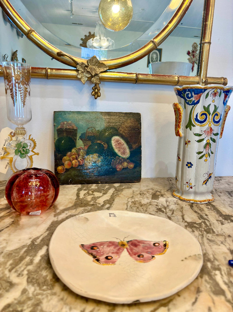 Decorative items including a vase, painting, and round plate with butterfly design on a marble surface.
