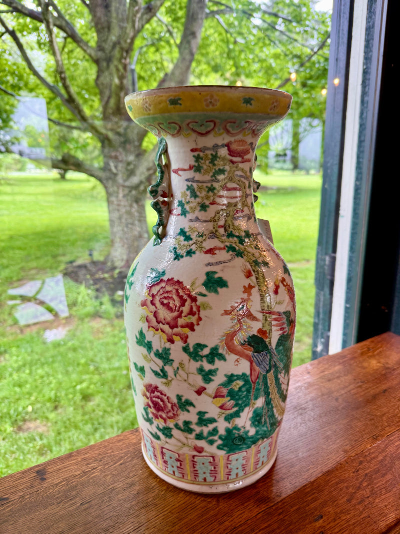 Decorative vase with floral and dragon design on a wooden surface outdoors.