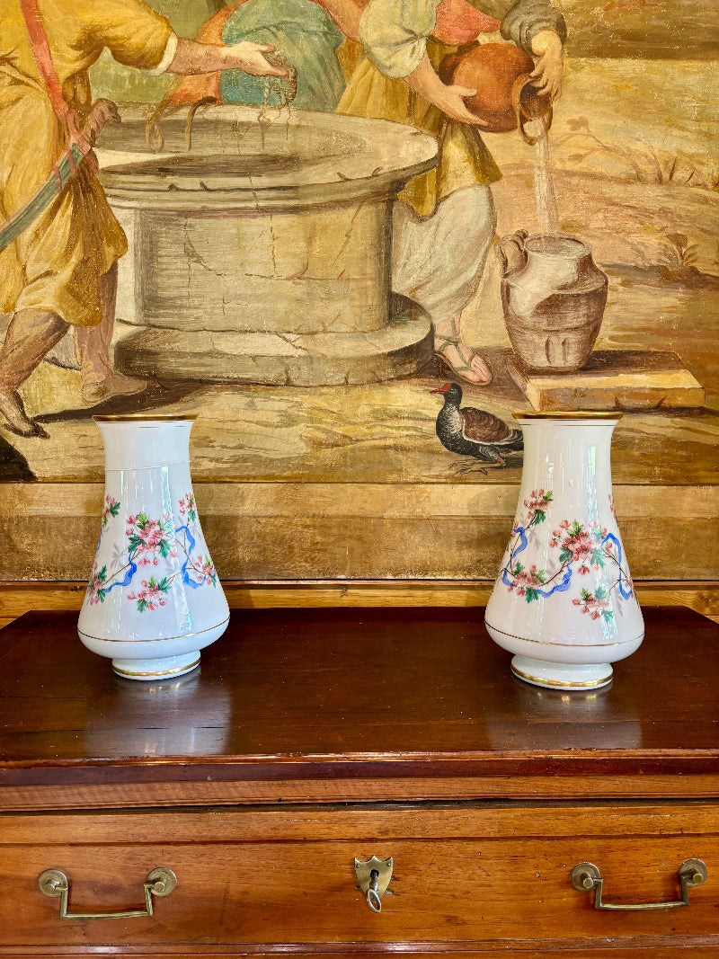 Two ceramic vases with floral designs on a wooden surface in front of a classical painting.
