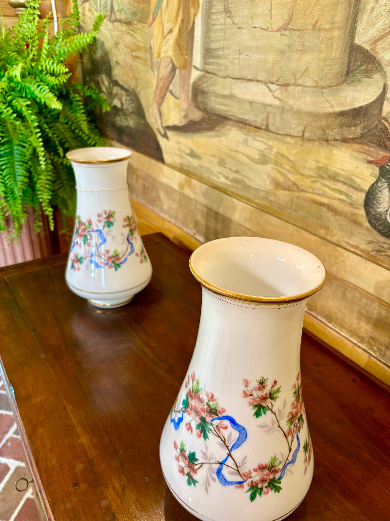 Two decorative vases with floral patterns on a wooden surface, with a painting in the background.
