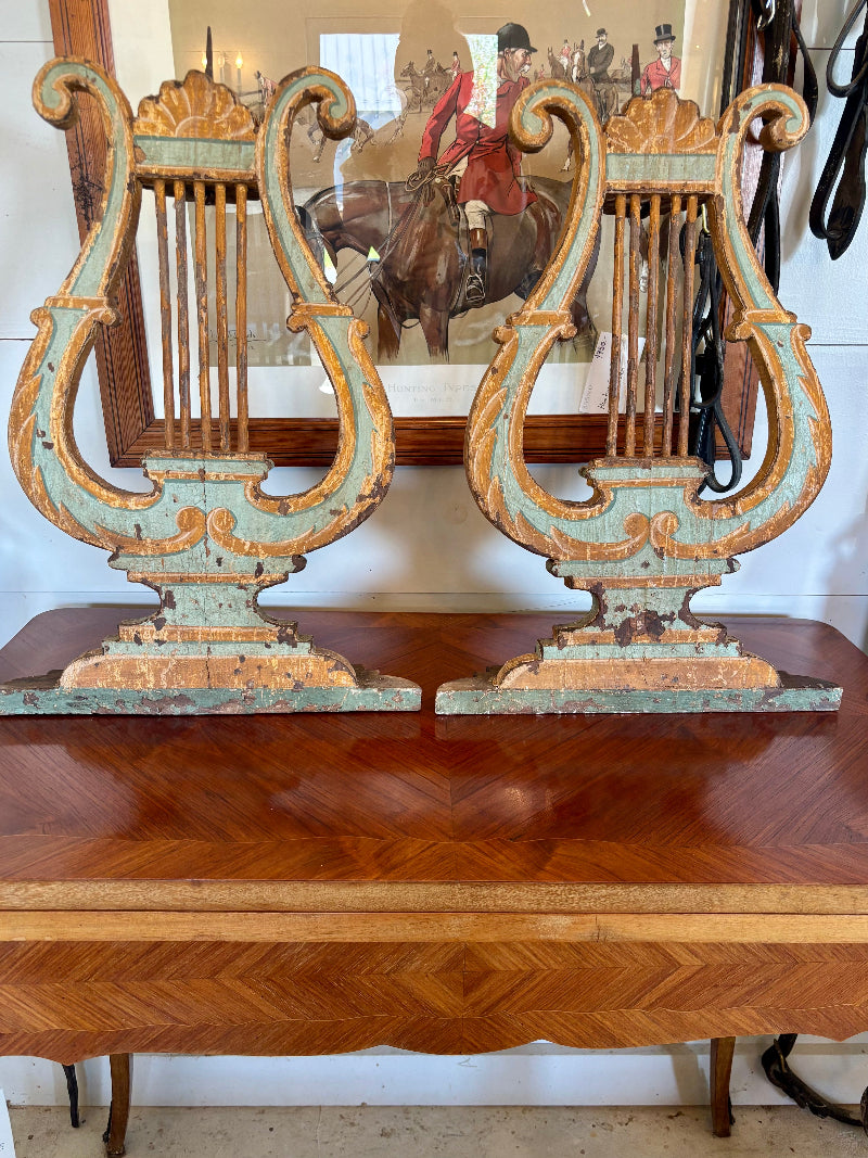 Decorative lyre-shaped candlesticks on a wooden surface with a painting of a horse and rider in the background.