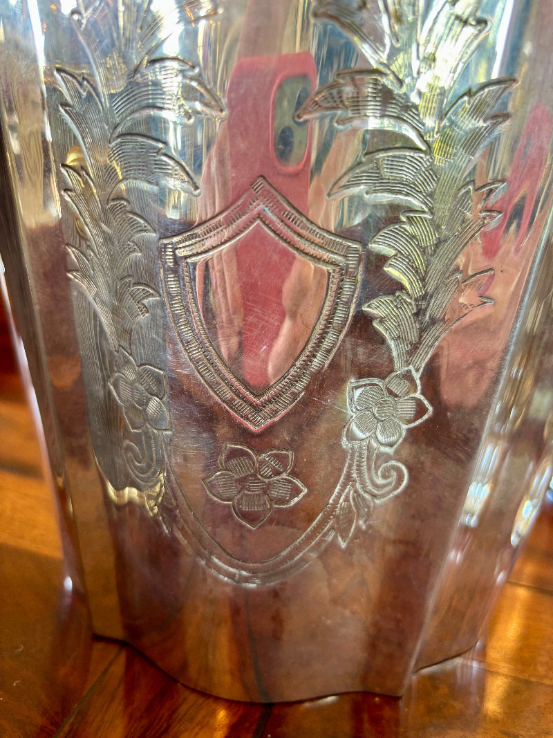 Decorative silver champagne bucket with engraved design on a wooden surface